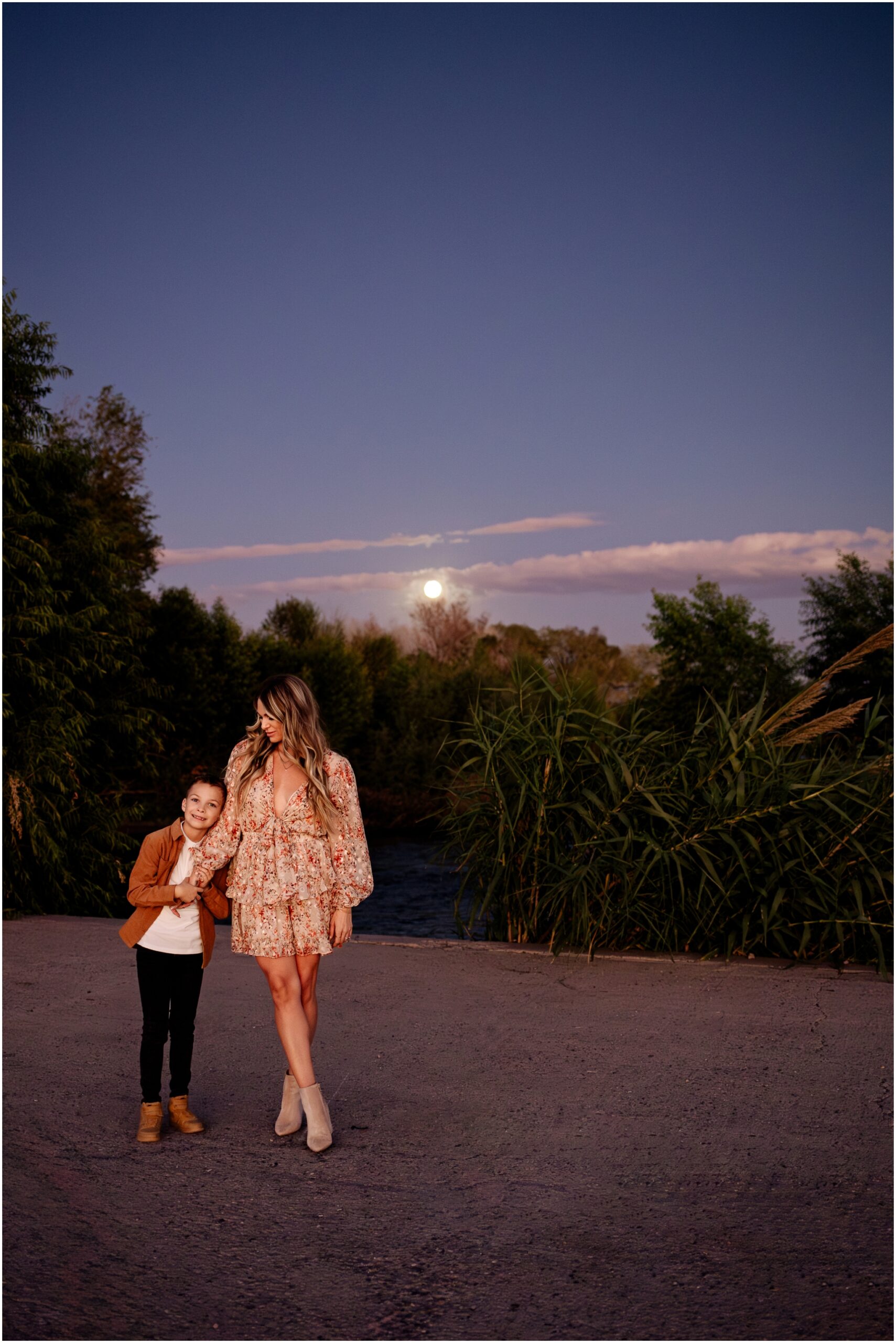 Stylish mother and son standing together in Arizona desert landscape  with moon shining during Phoenix lifestyle family photoshoot